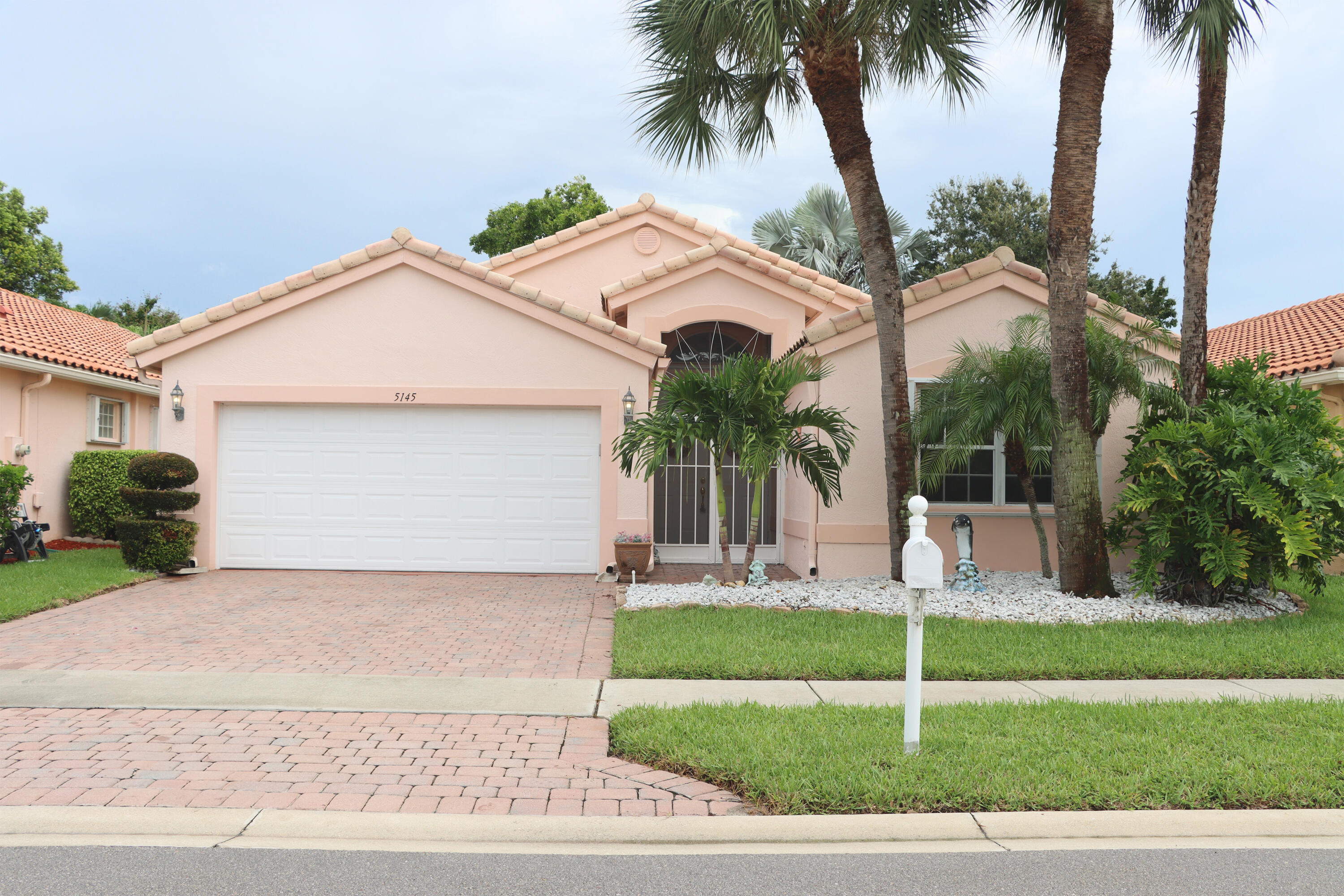 a front view of a house with a garden and palm trees