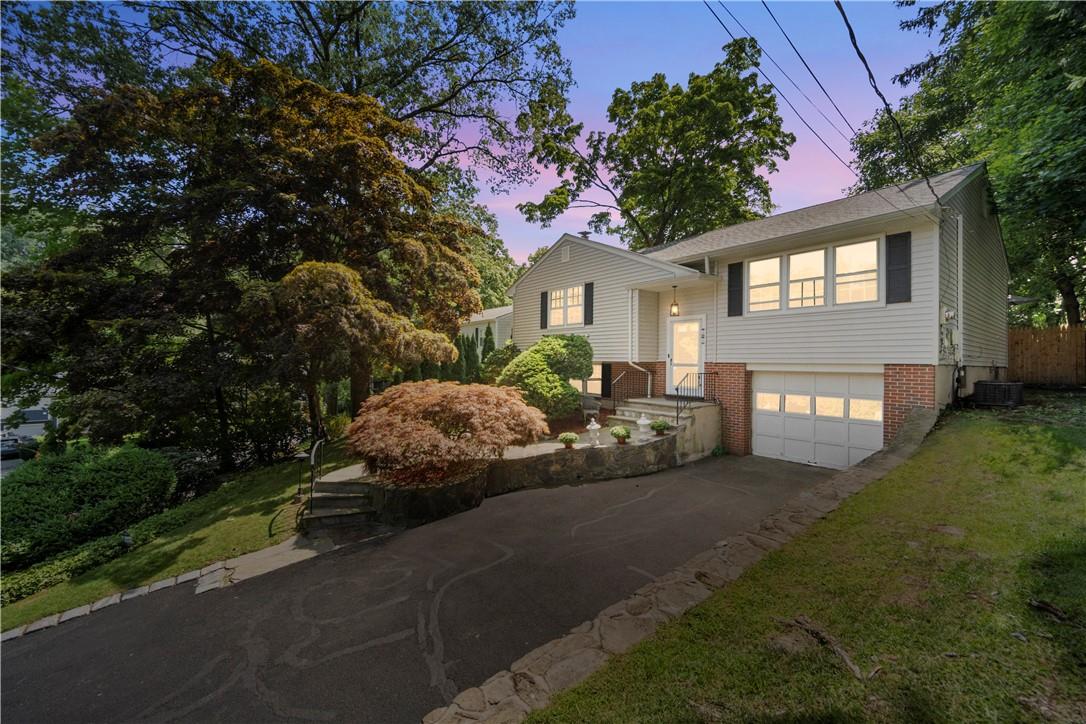 Raised ranch featuring a lawn, central AC unit, and a garage