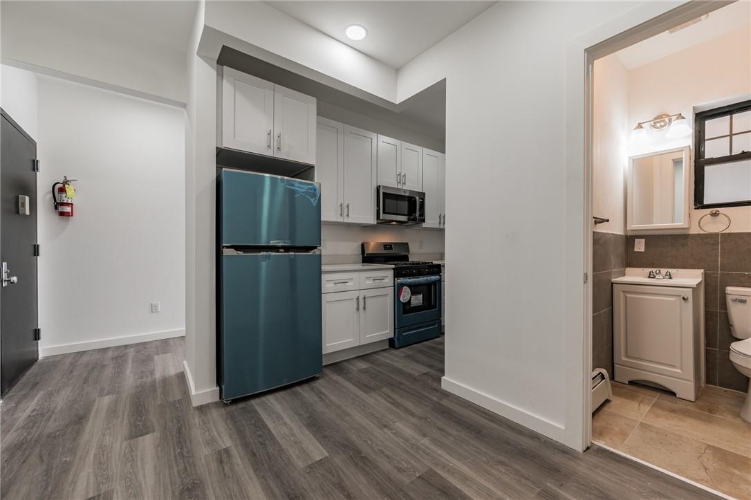 Kitchen featuring appliances with stainless steel finishes, a baseboard radiator, white cabinetry, tile walls, and dark wood-type flooring