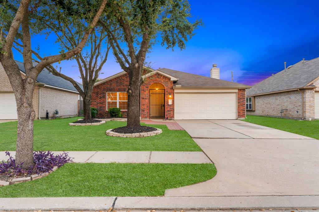 This is a single-story brick home featuring a two-car garage, a well-maintained lawn, and mature landscaping with a tree in the front yard.