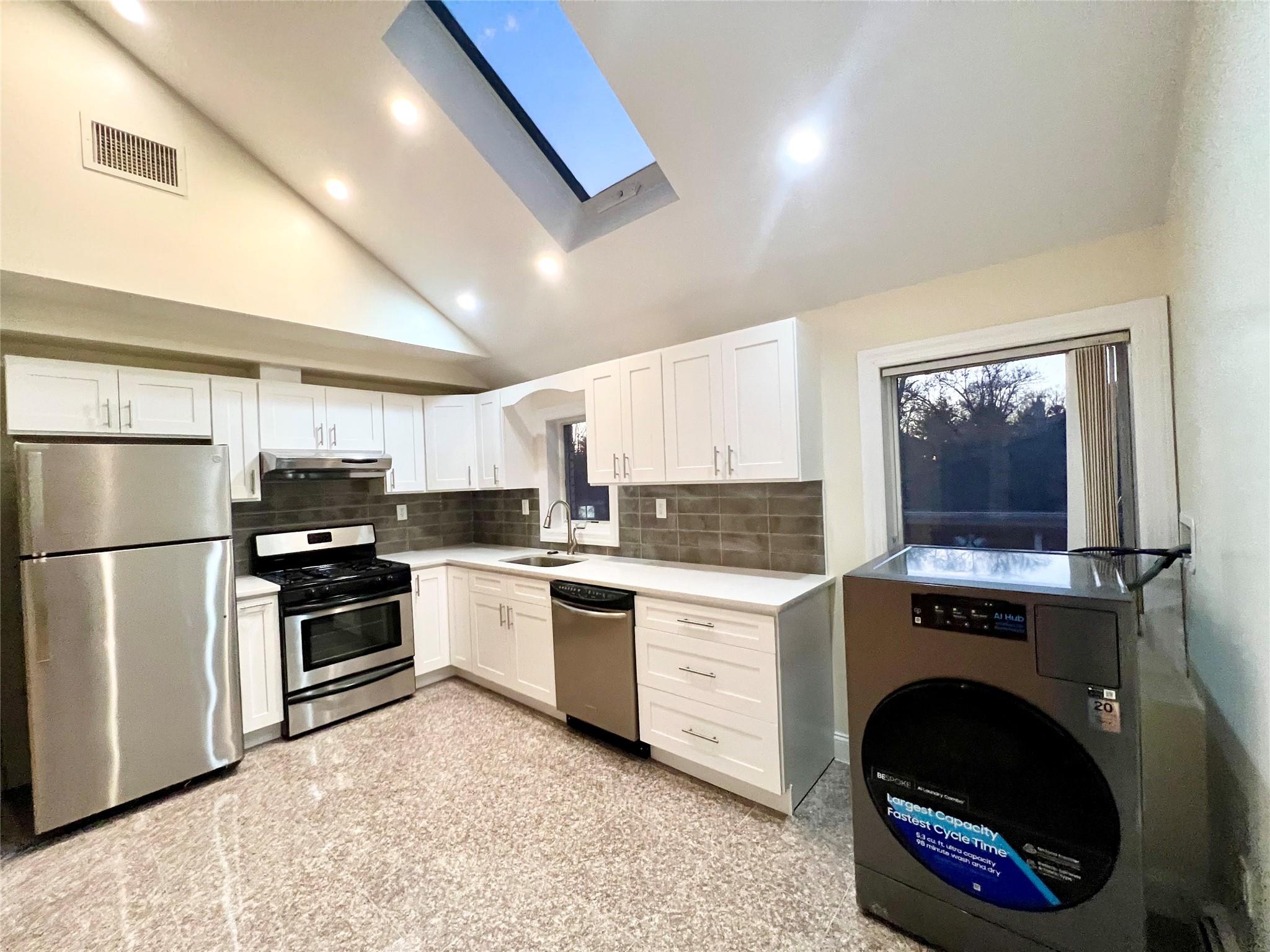 Kitchen with vaulted ceiling with skylight, stainless steel appliances, sink, white cabinets, and washer / dryer