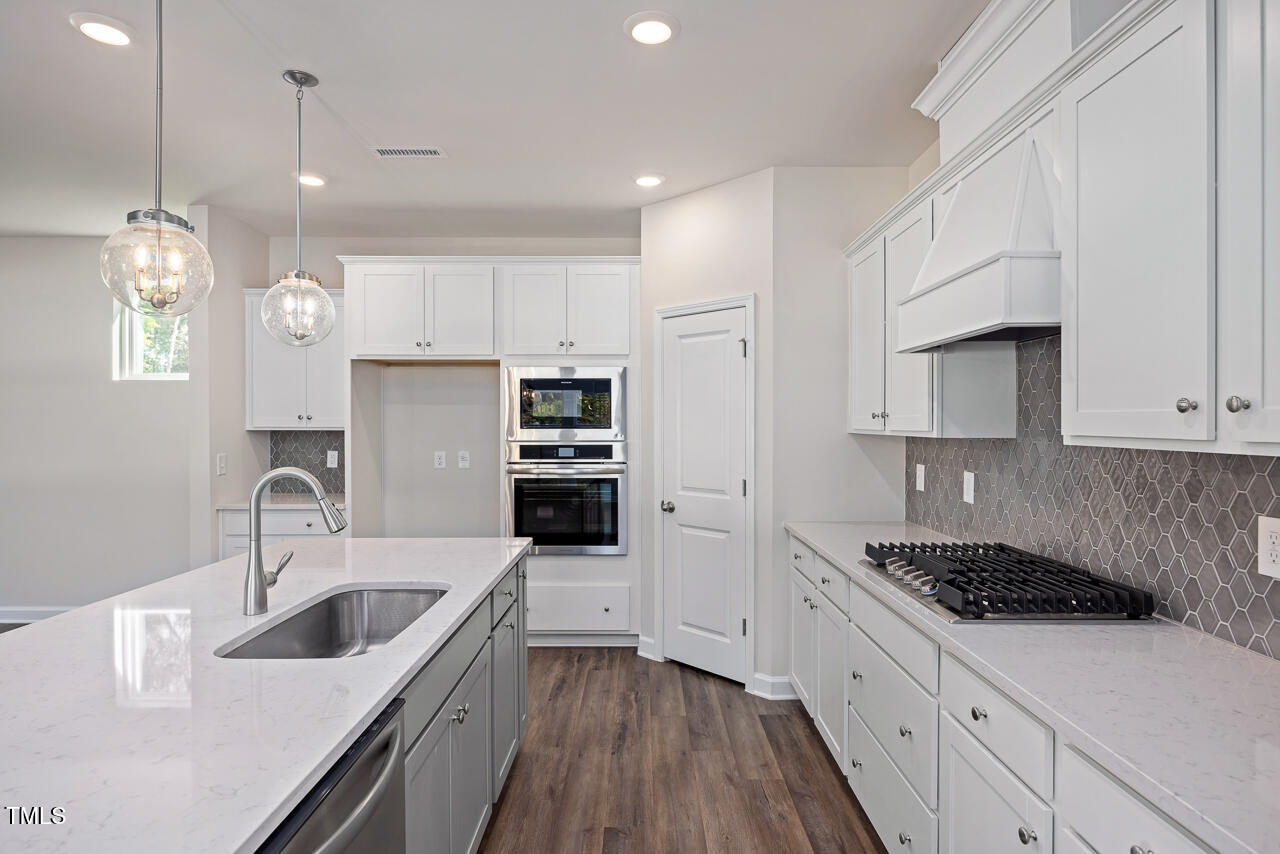 a kitchen with stainless steel appliances a sink stove and white cabinets with wooden floor