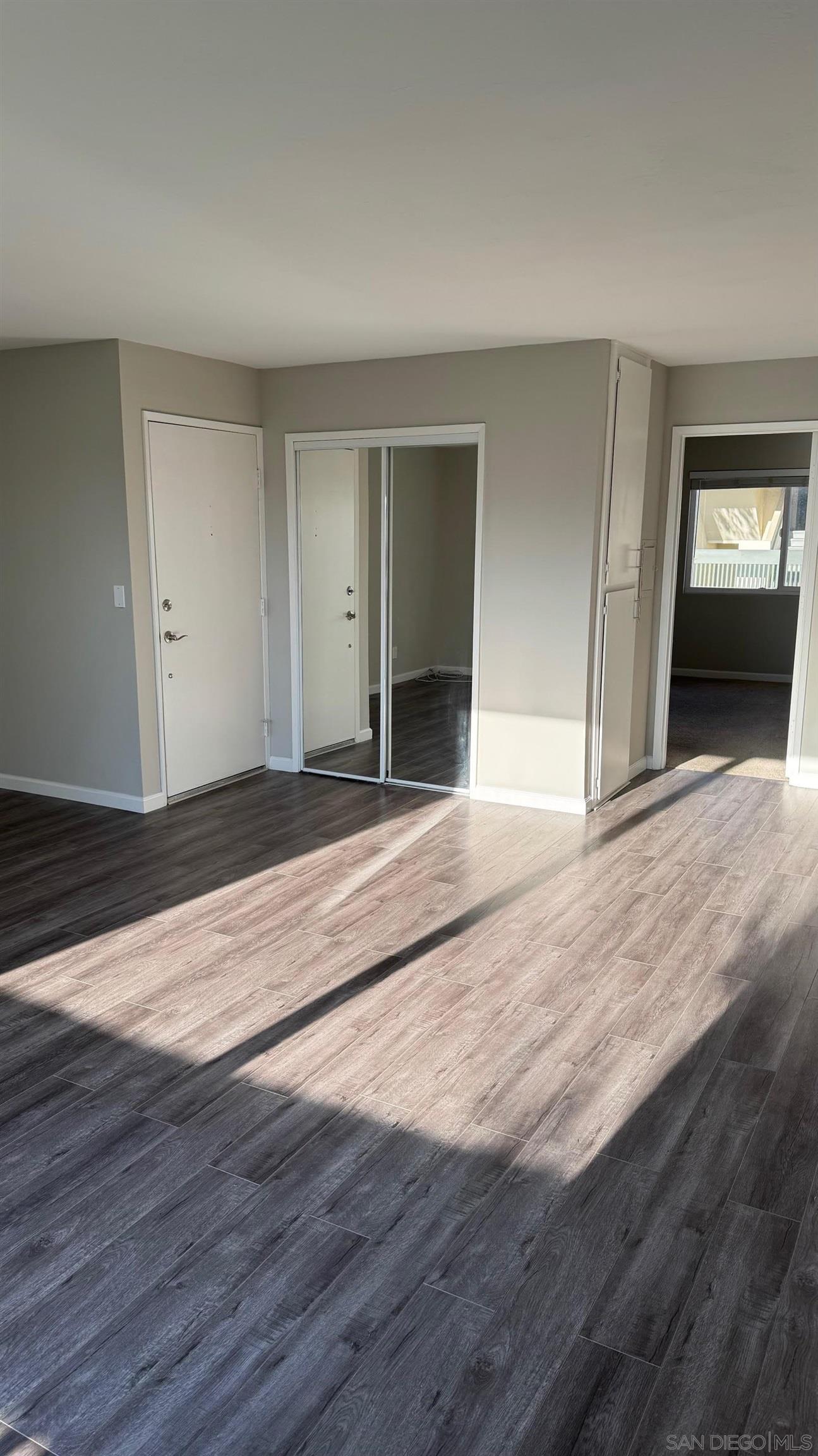 a view of an empty room with wooden floor and kitchen