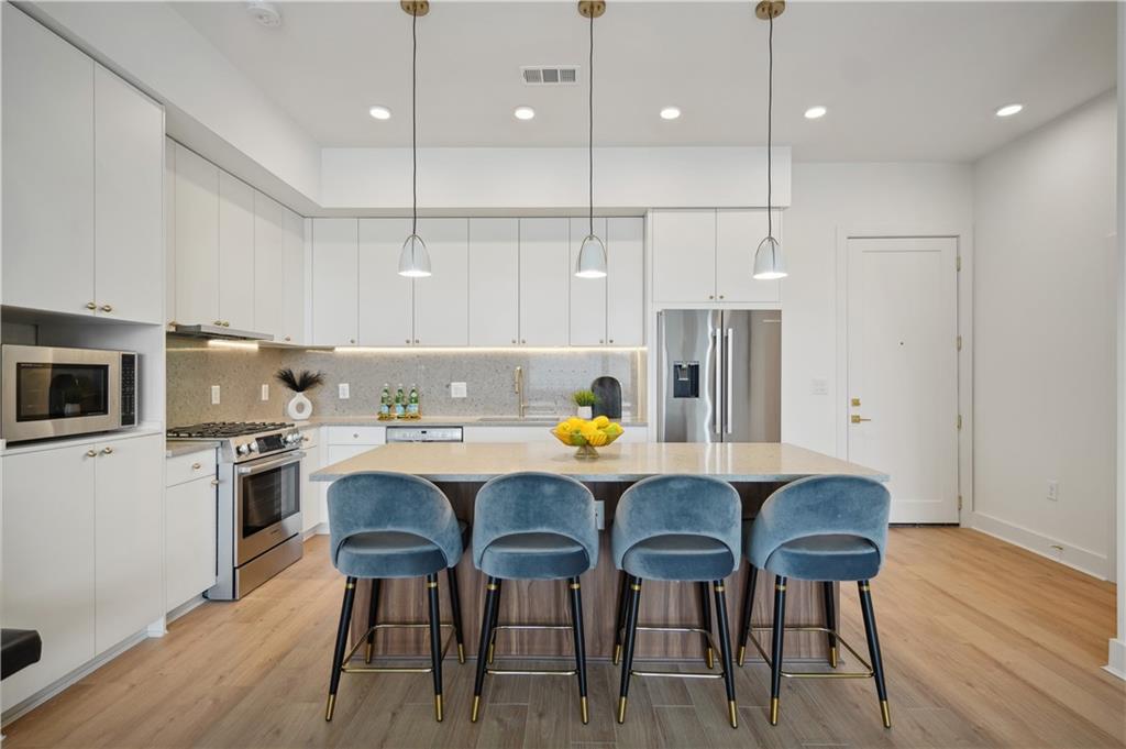 a kitchen with stainless steel appliances granite countertop a stove a refrigerator a kitchen island a dining table and chairs with wooden floor