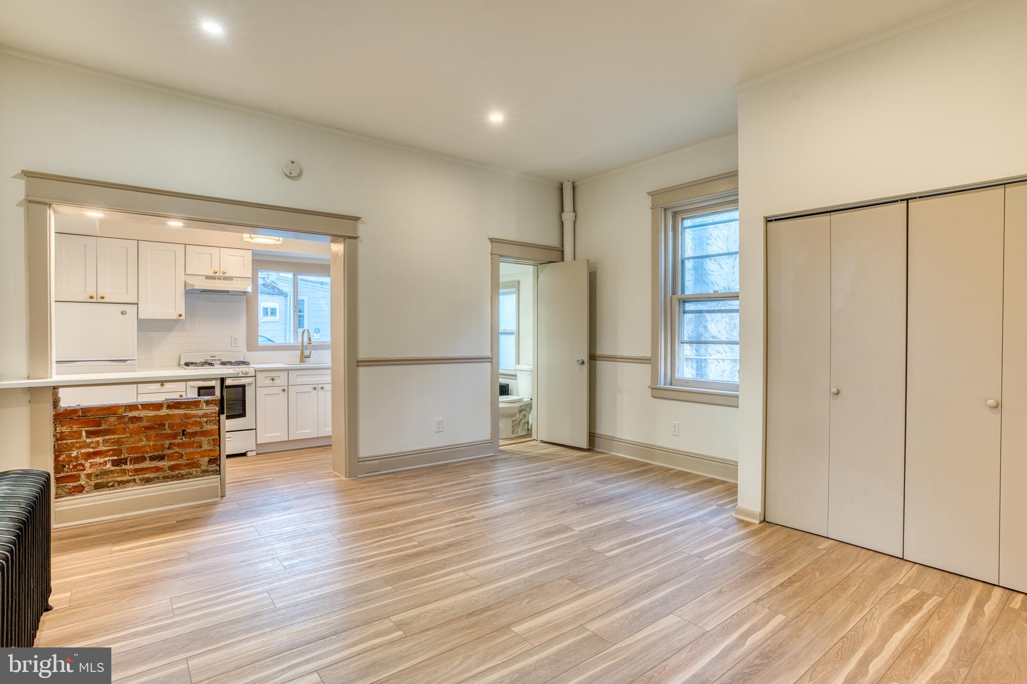 an empty room with wooden floor kitchen view and a window