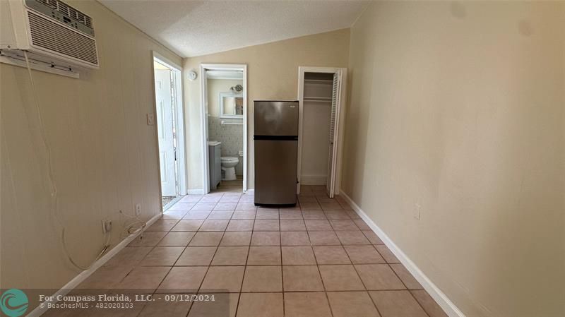 a view of a refrigerator in kitchen and an empty room in wooden floor