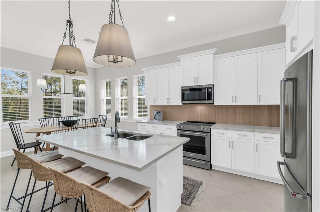 Kitchen featuring sink, hanging light fixtures, an island with sink, white cabinets, and appliances with stainless steel finishes