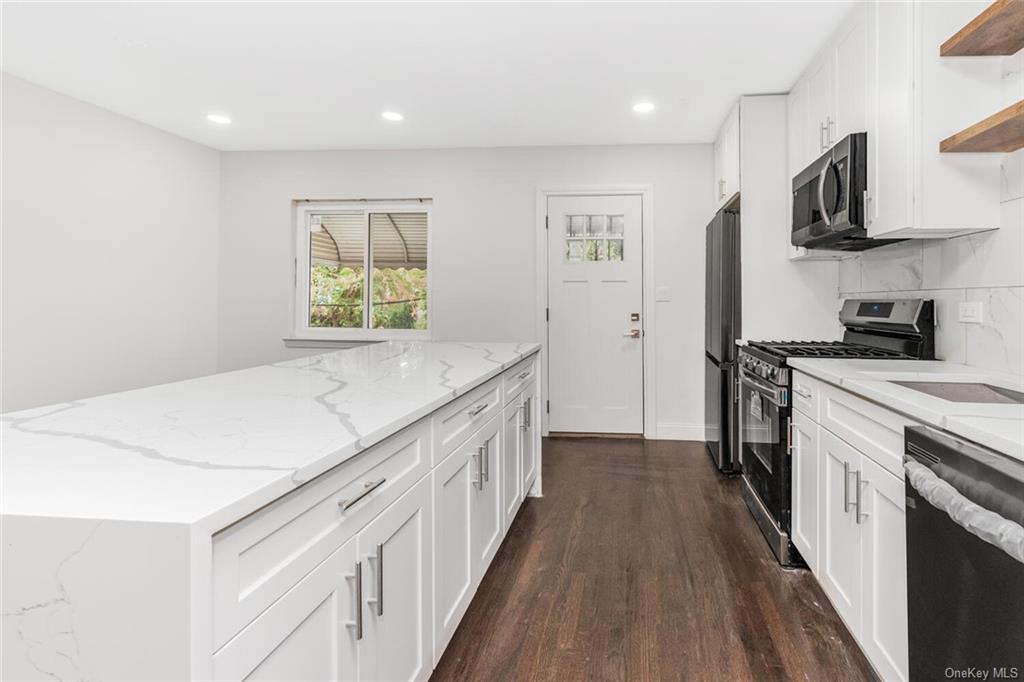 Kitchen featuring dark hardwood / wood-style floors, white cabinetry, backsplash, appliances with stainless steel finishes, and light stone countertops