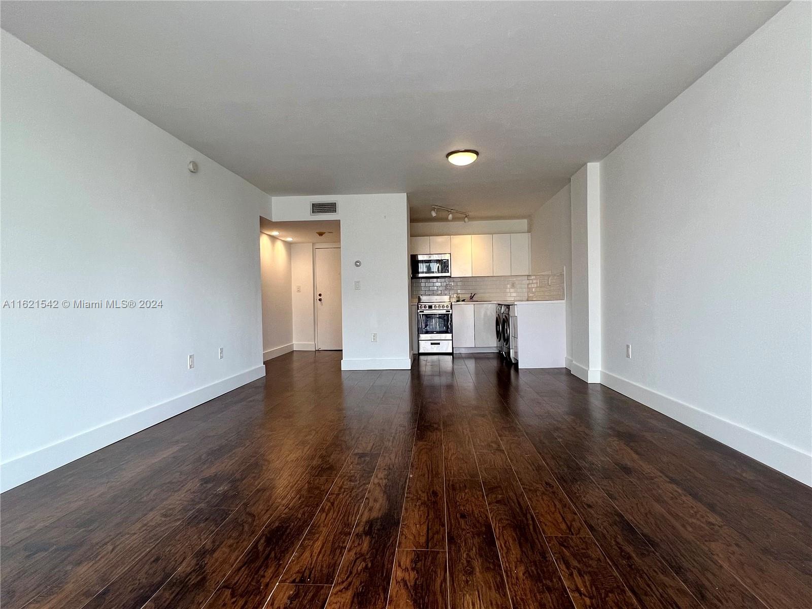 a view of empty room with wooden floor and kitchen view