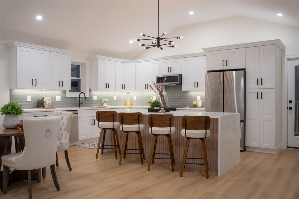 a kitchen with kitchen island a dining table chairs refrigerator and cabinets