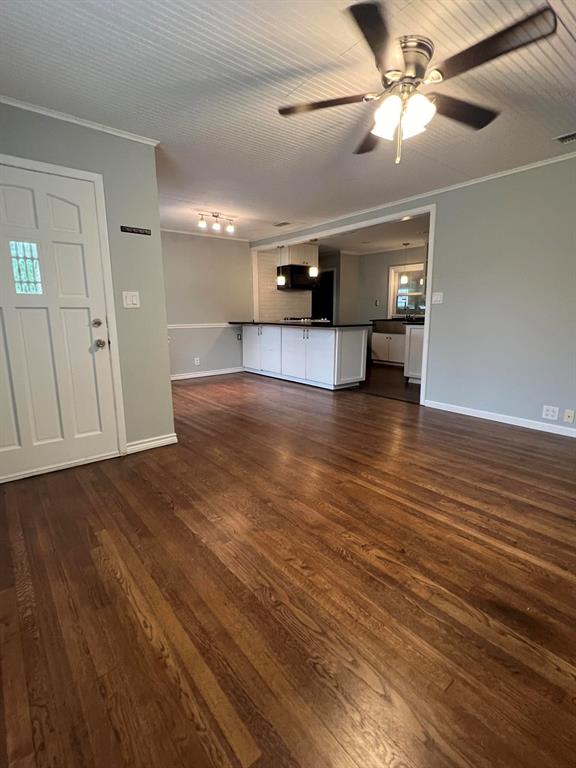 a view of an empty room with wooden floor and a ceiling fan