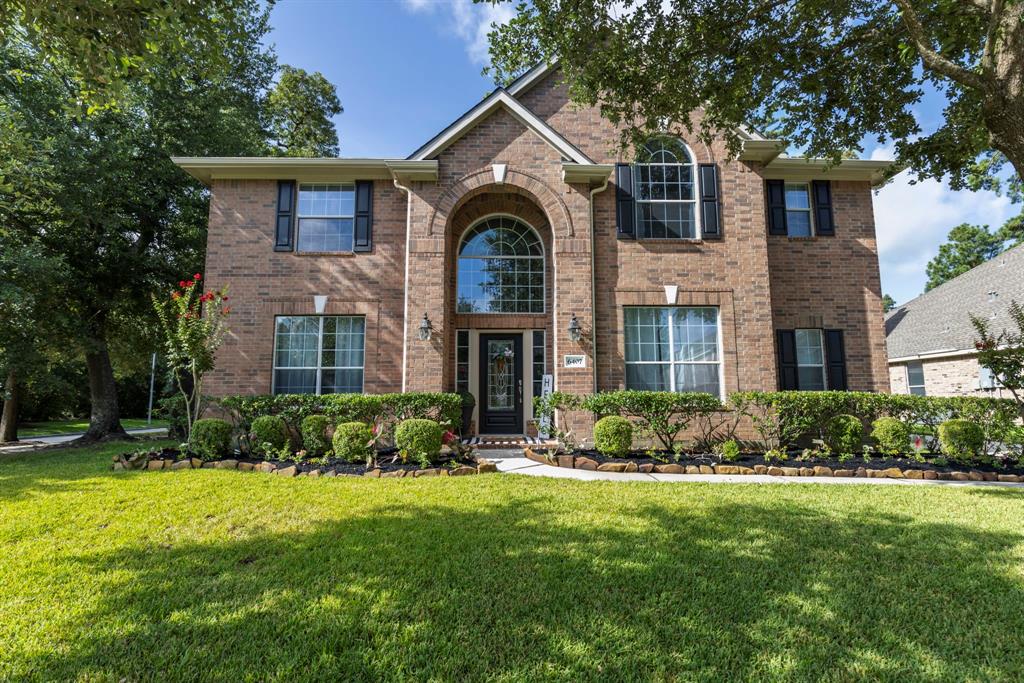 This is a two-story brick home featuring large windows, a well-maintained lawn, and mature trees, offering both curb appeal and privacy.