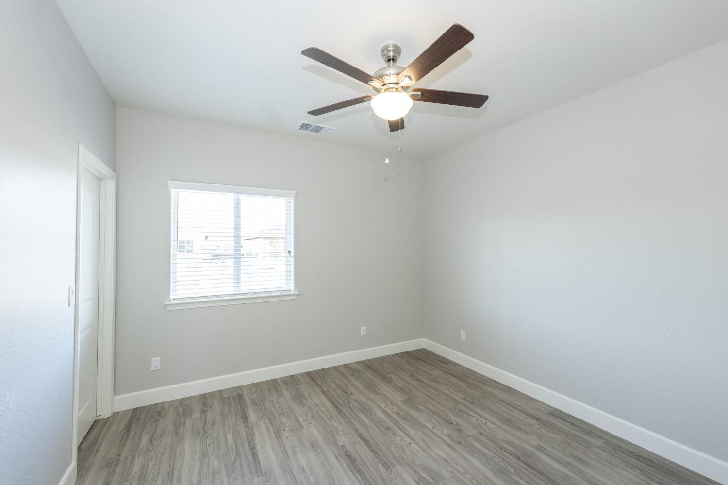 an empty room with wooden floor ceiling fan and windows