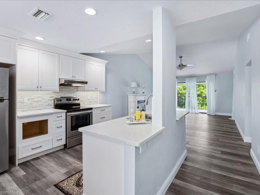 Kitchen featuring appliances with stainless steel finishes, dark wood-type flooring, decorative backsplash, and vaulted ceiling