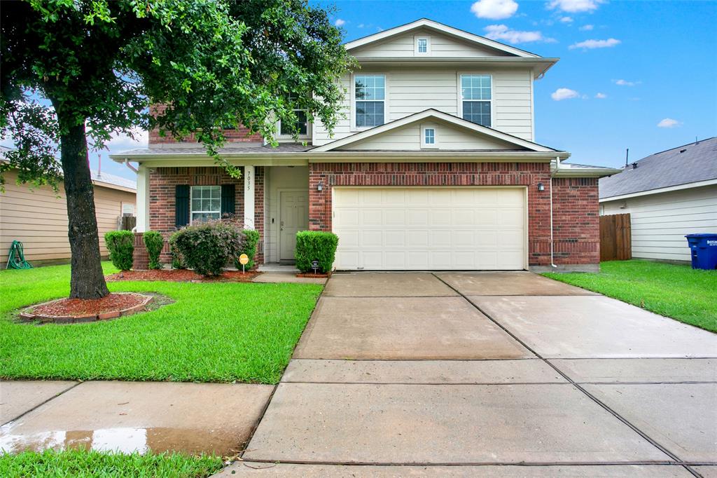 Charming two-story home with classic brick exterior, featuring a spacious attached garage for two cars, set amidst a well-maintained lawn and mature, inviting landscape.