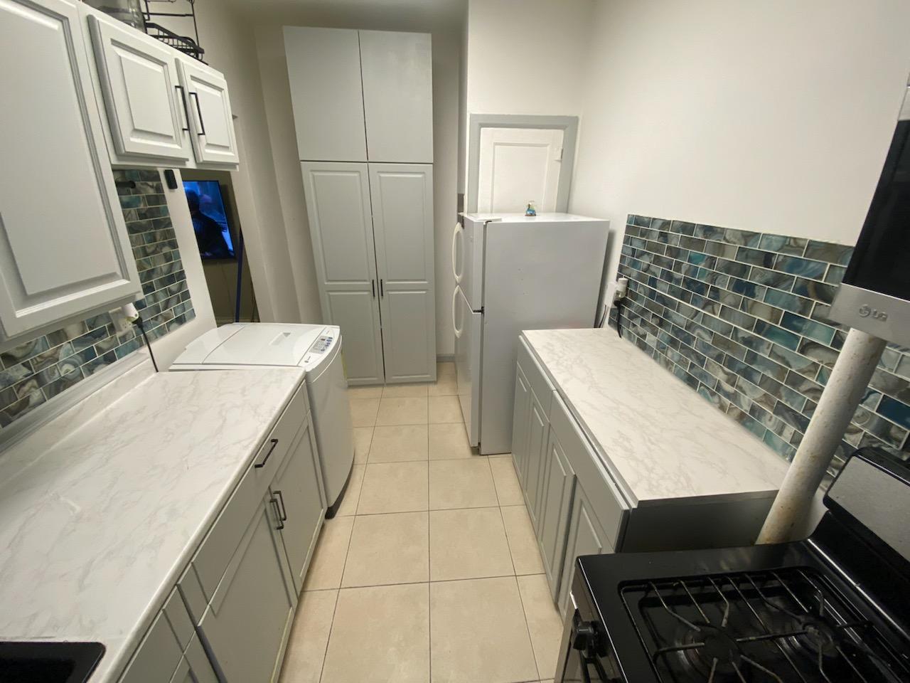 Kitchen with white cabinets, marble counters, glass design backsplash, light cabinets, tiled floor, pantry, full size washer.