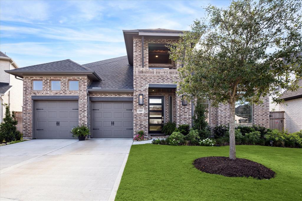 This is a two-story brick home featuring a well-manicured lawn, a mature tree in the front yard, and a 3 car tandem. 