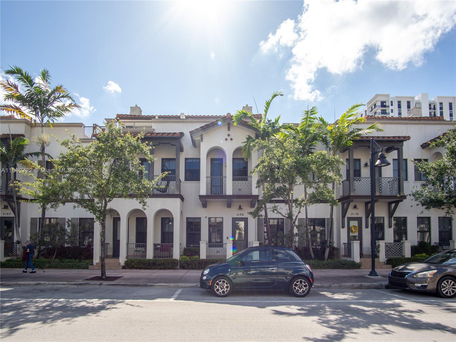 a front view of a building with lot of cars and trees