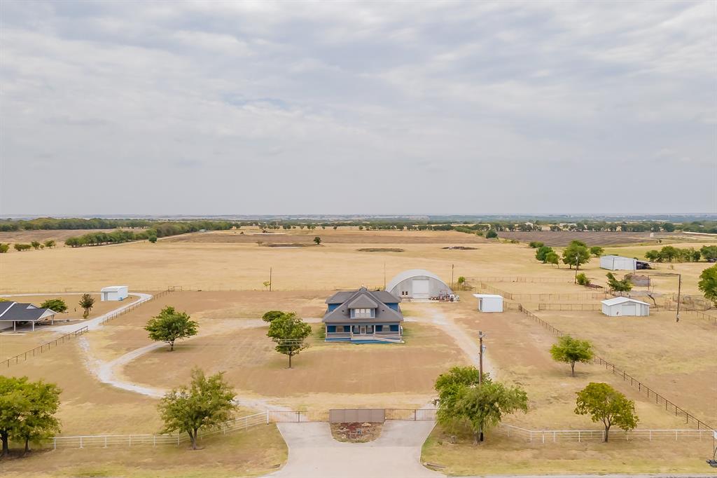 This aerial image shows the spacious property with a single-family home, featuring a large front yard, an expansive workshop and other outbuildings, set amid expansive open fields, offering unobstructed views, privacy, and rural charm. Property includes TWO 500 gallon septic tanks.  Rhome is an easy commute from Dallas area and only 12 miles from Texas Motor speedway so great primary residence, weekend getaway, or EXCELLENT investment opportunity!