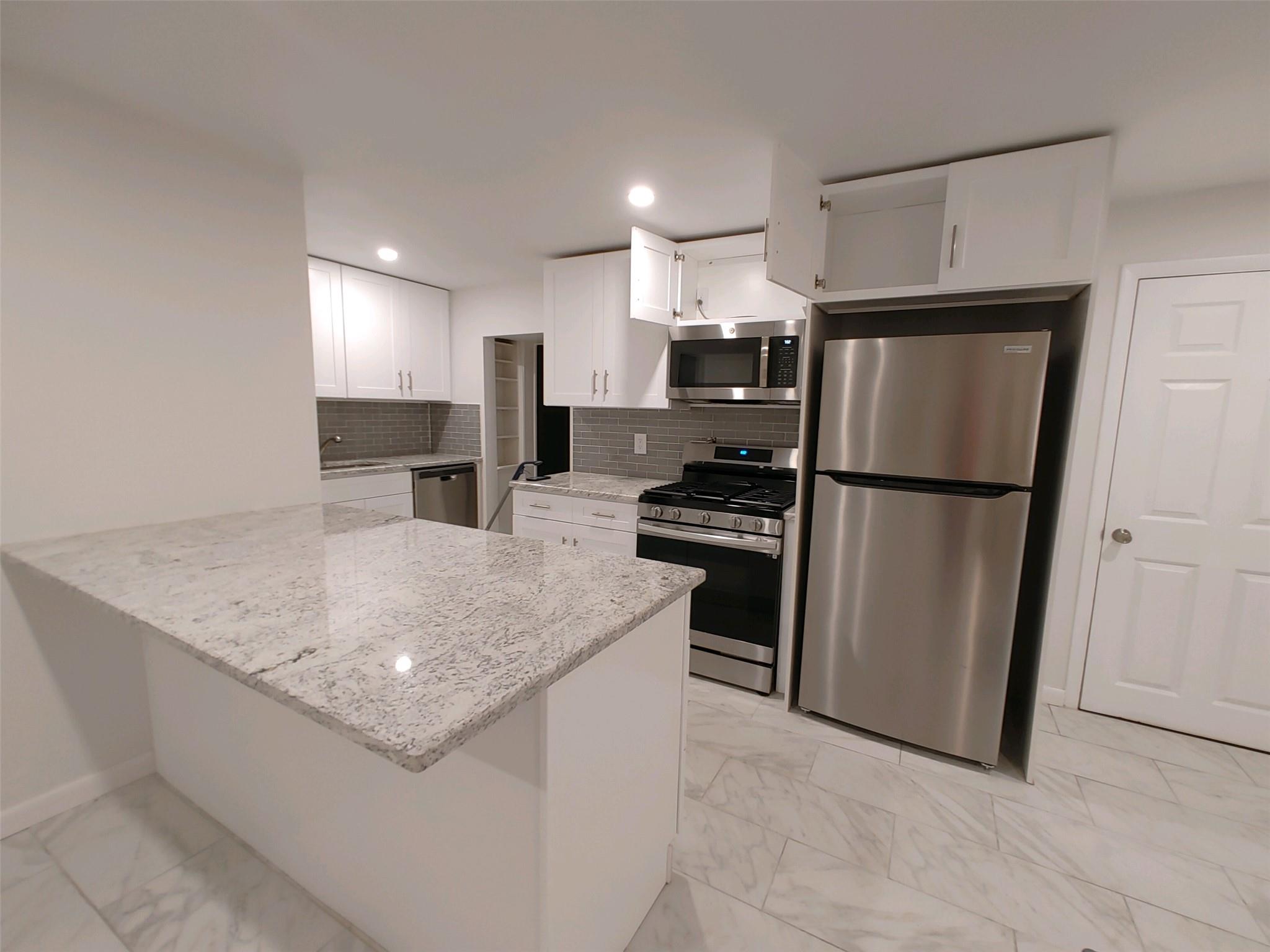 Kitchen with kitchen peninsula, light stone countertops, backsplash, stainless steel appliances, and white cabinets