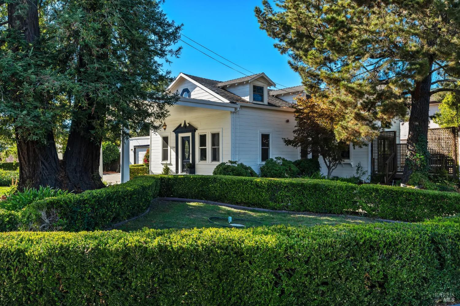 a view of a white house next to a yard with big trees