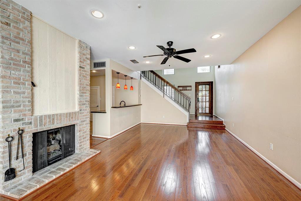 This is a spacious living area featuring hardwood floors, a brick fireplace, a ceiling fan, and an open layout with direct access to the kitchen. 