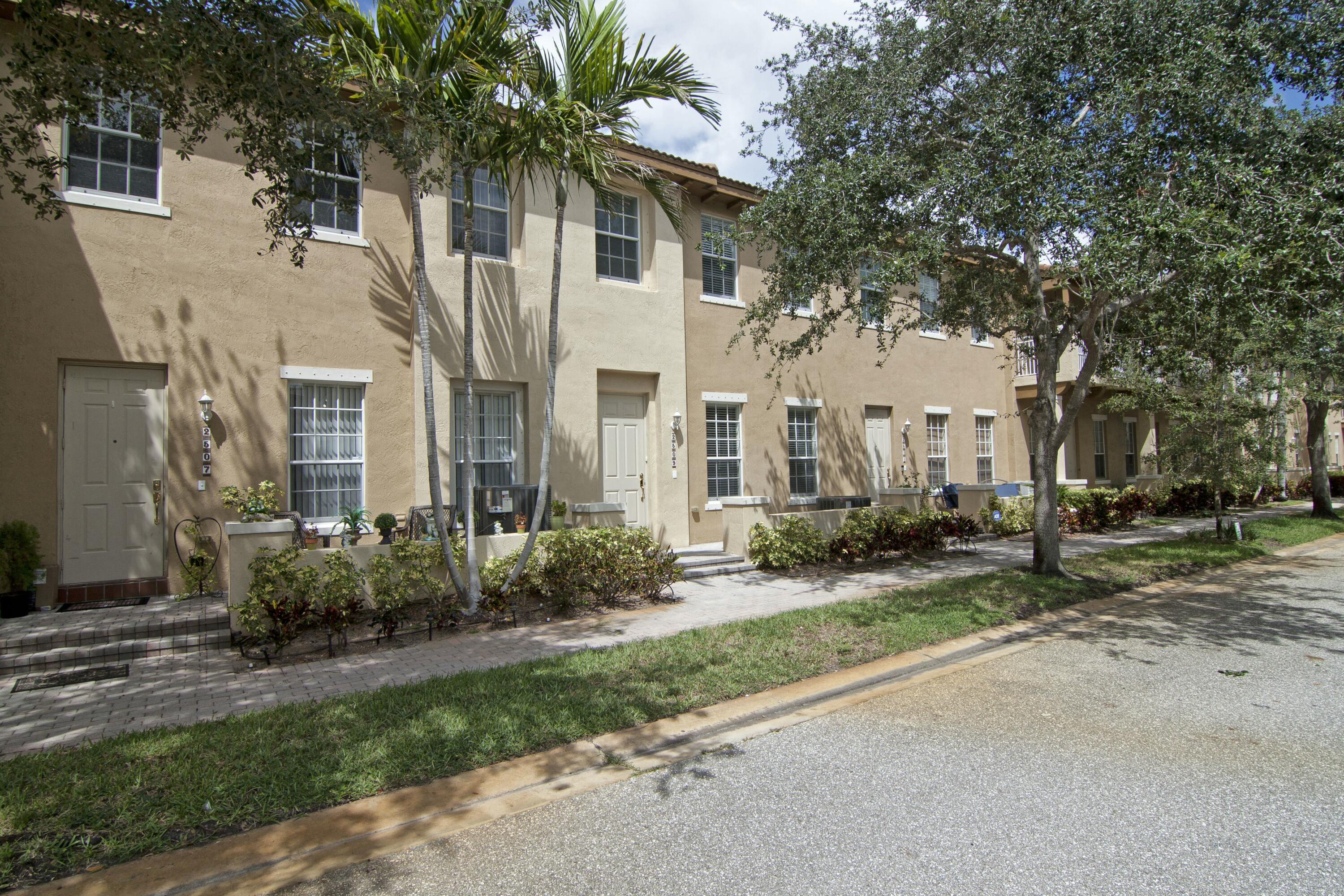 a view of a white house next to a yard with plants and trees