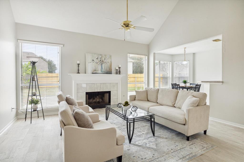 A stunning living room with high ceilings and large windows that fill the space with natural light. The open-concept design seamlessly connects to the dining area, creating an ideal layout for entertaining. The wood-look tile flooring adds a modern touch, while the soft neutral tones provide a timeless and inviting ambiance.