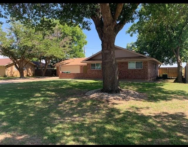 a backyard of a house with plants and large tree