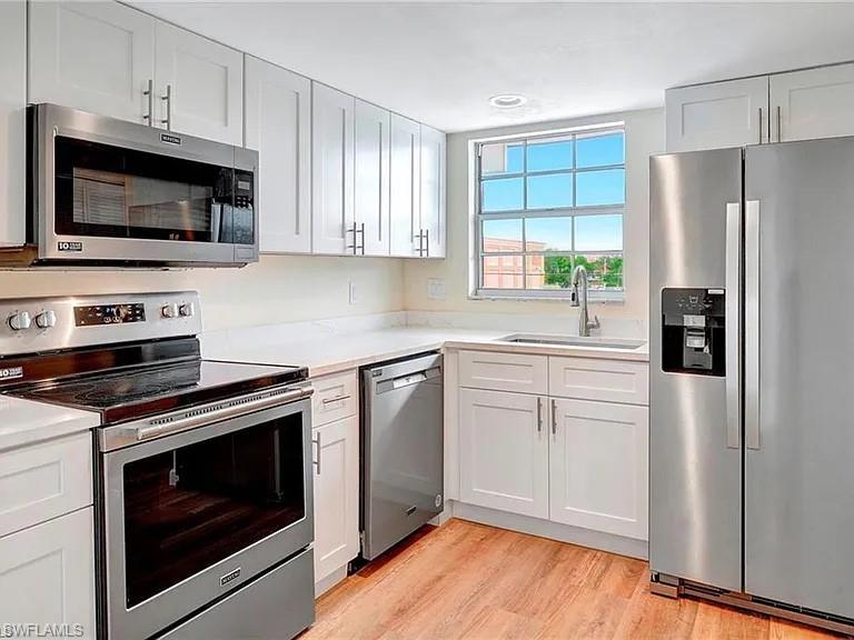 Kitchen featuring sink, light stone countertops, light wood-type flooring, white cabinetry, and stainless steel appliances