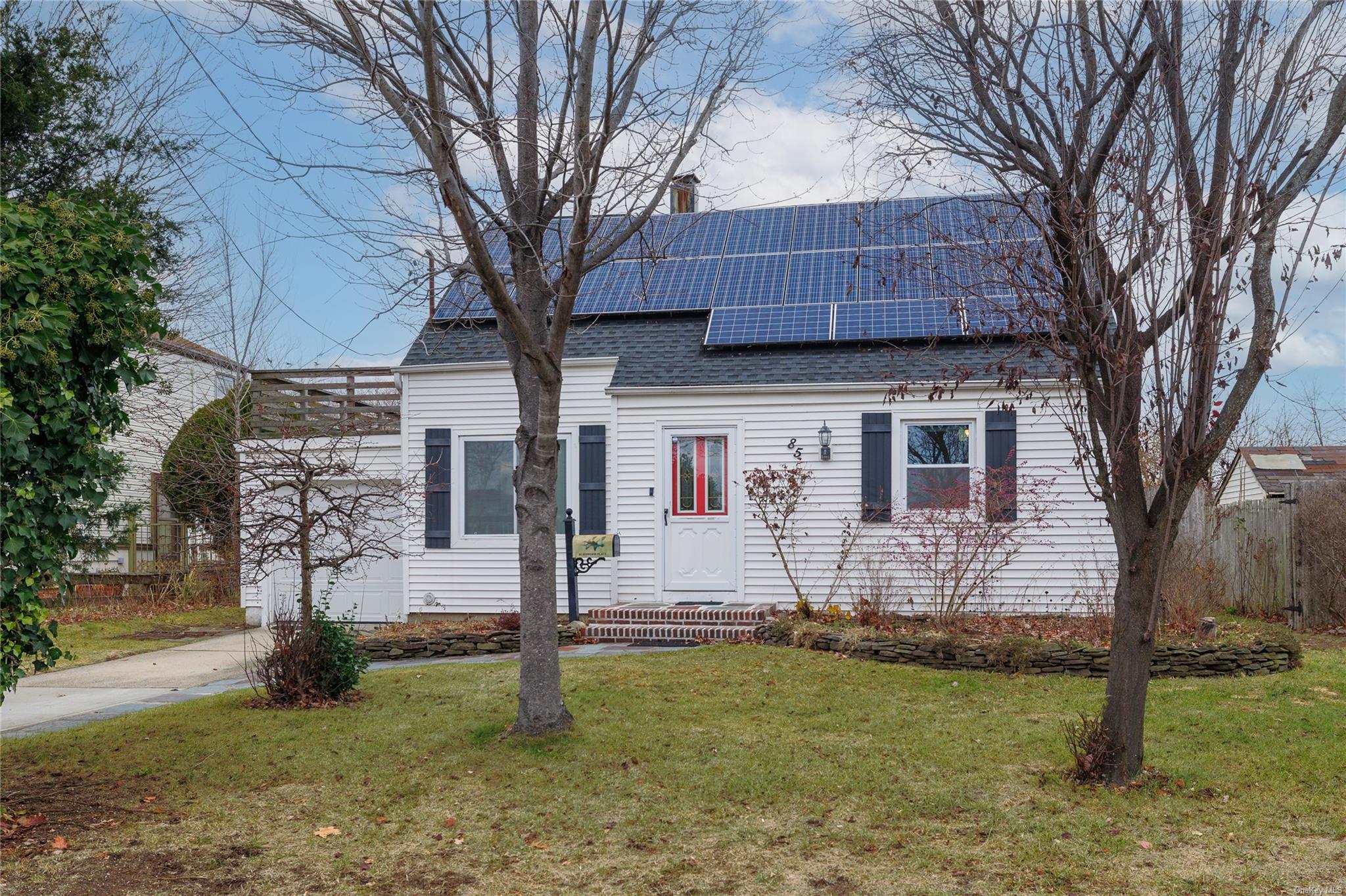 Cape cod style home featuring a front lawn and solar panels