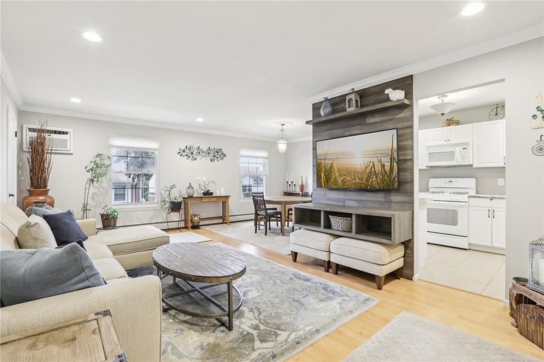 Living room with ornamental molding, a wall unit AC, and light hardwood / wood-style floors