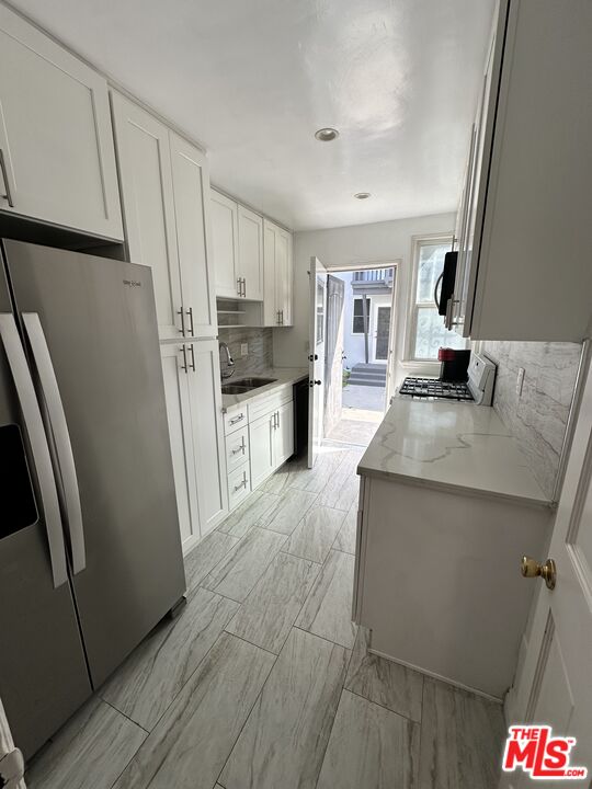 a kitchen with granite countertop a refrigerator a sink a stove and cabinets