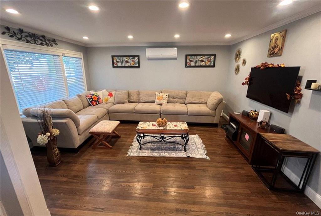 Living room featuring dark wood-type flooring, crown molding, and a wall mounted AC