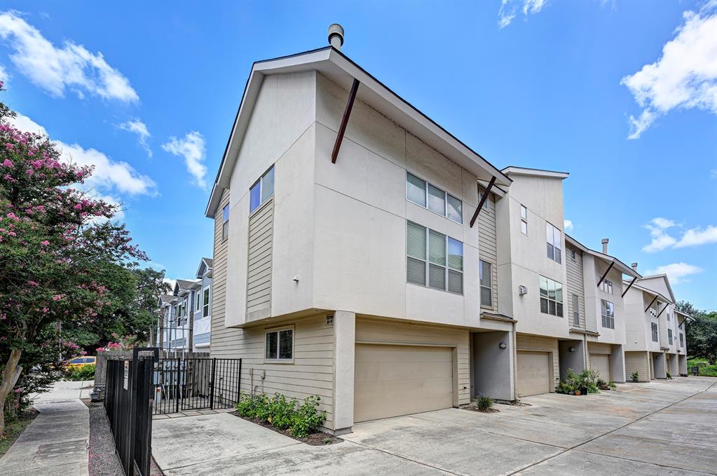 Modern multi-story townhome featuring spacious two-car garage, large windows, and a secure gated entrance. Additional parking on the side of the unit for a third car.