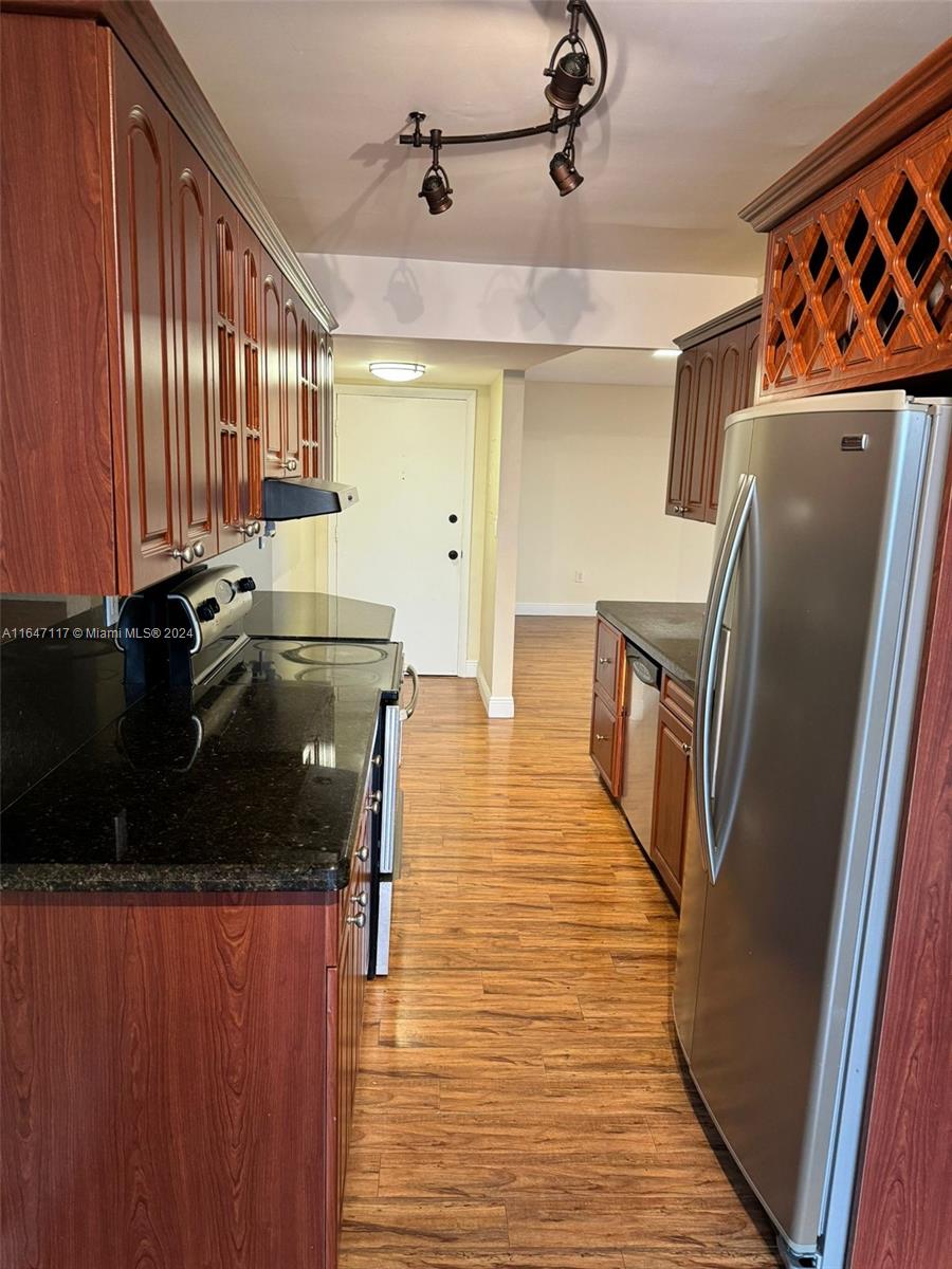 a kitchen with stainless steel appliances granite countertop a refrigerator a stove and a sink with wooden floor