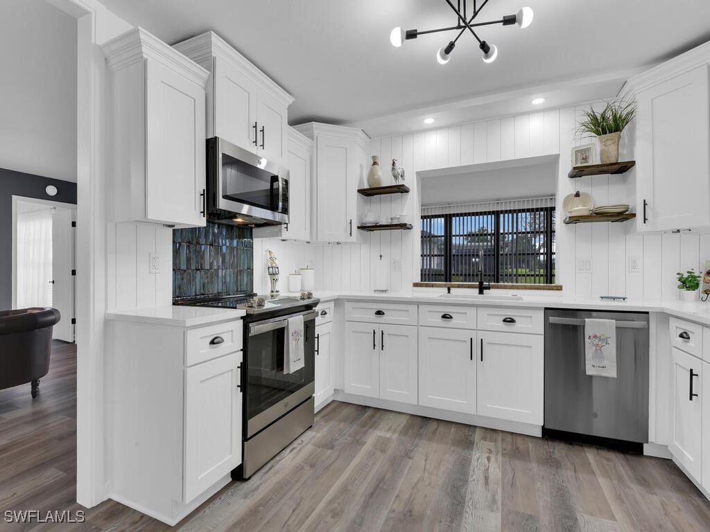 a kitchen with stainless steel appliances white cabinets a sink a stove a microwave and wooden floors