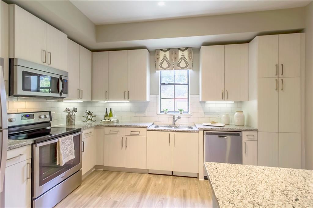 a kitchen with stainless steel appliances granite countertop a stove top oven a sink dishwasher and white cabinets with wooden floor