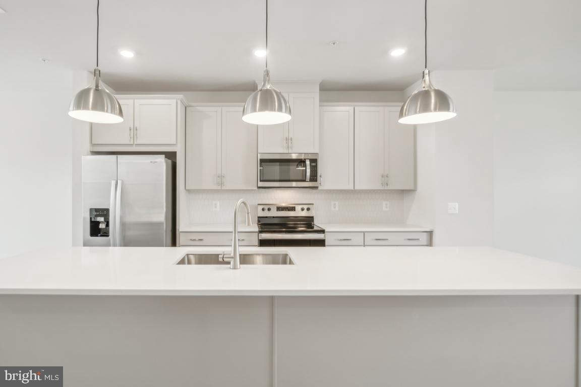 a kitchen with stainless steel appliances a sink a stove a refrigerator and white cabinets