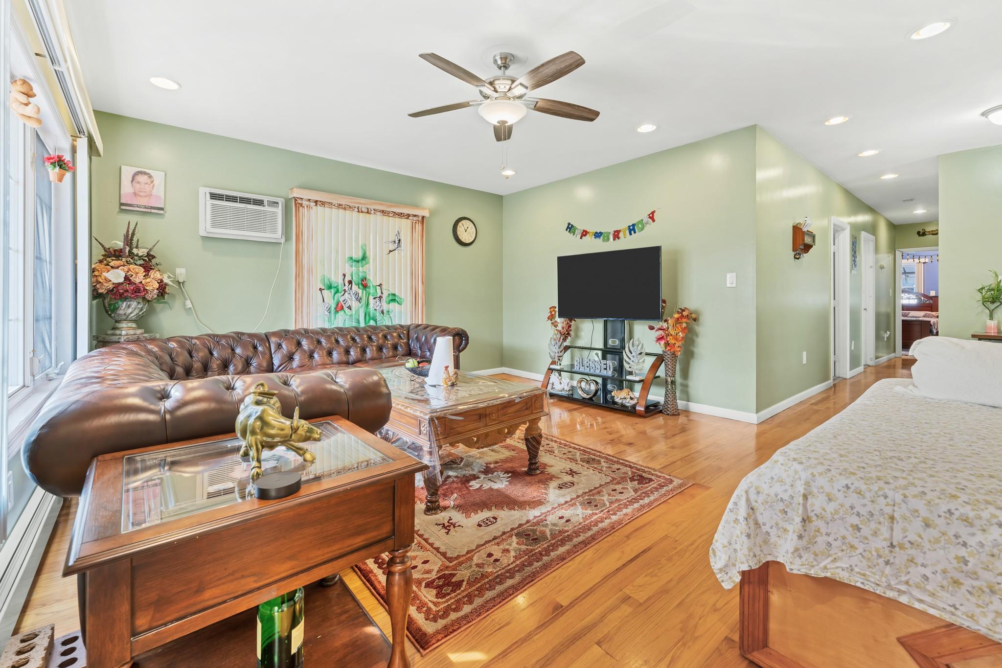 Living room with a wall mounted AC, ceiling fan, and light hardwood / wood-style floors