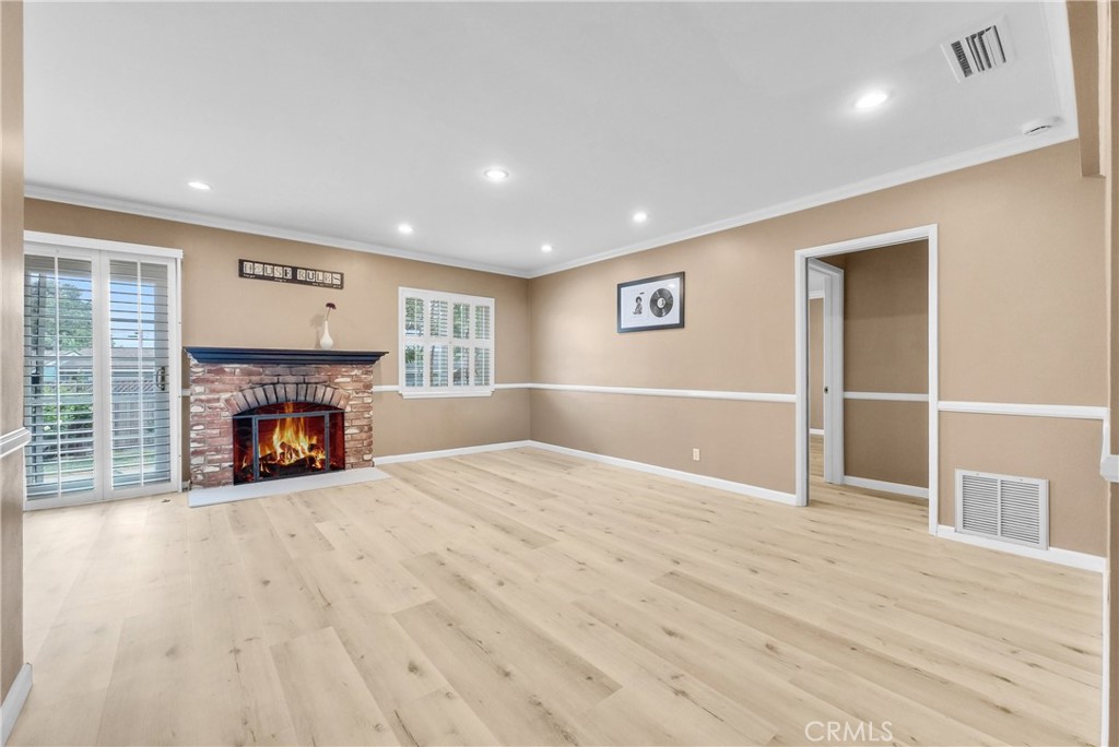 a view of an empty room with wooden floor fireplace and a window