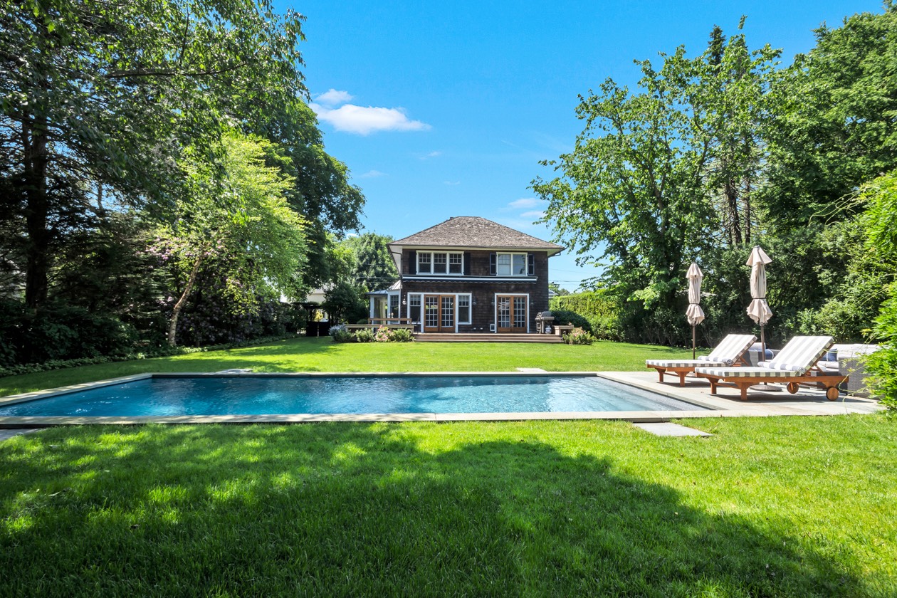 a view of a swimming pool with lawn chairs and large trees