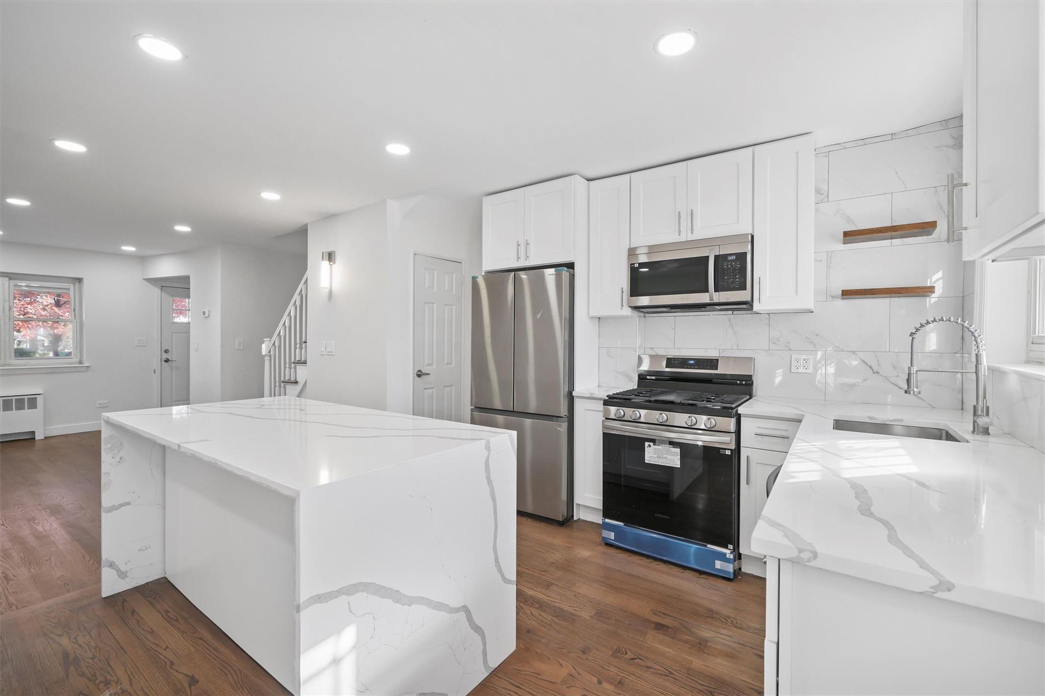 Kitchen with white cabinetry, sink, a center island, stainless steel appliances, and light stone counters