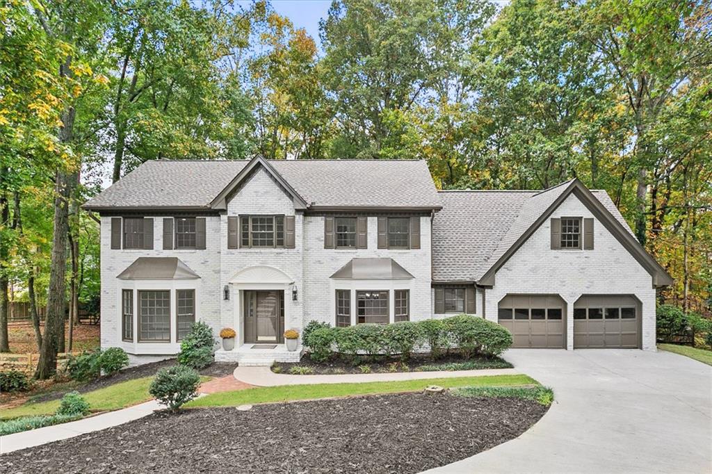 a white house with a yard plants and large tree