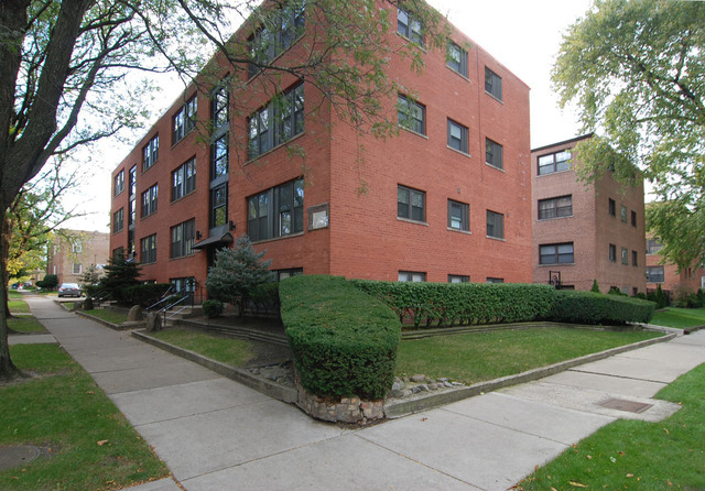 a front view of a multi story residential apartment building with yard and green space