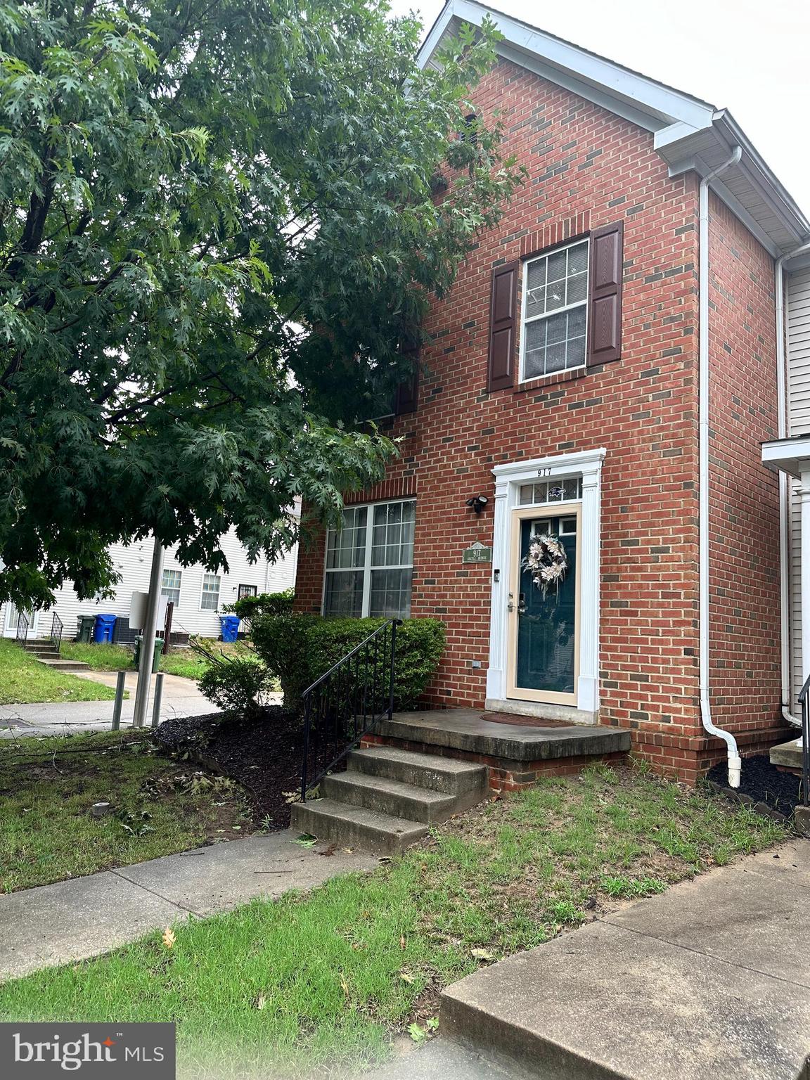 a view of a brick house with a yard potted plants and a large tree