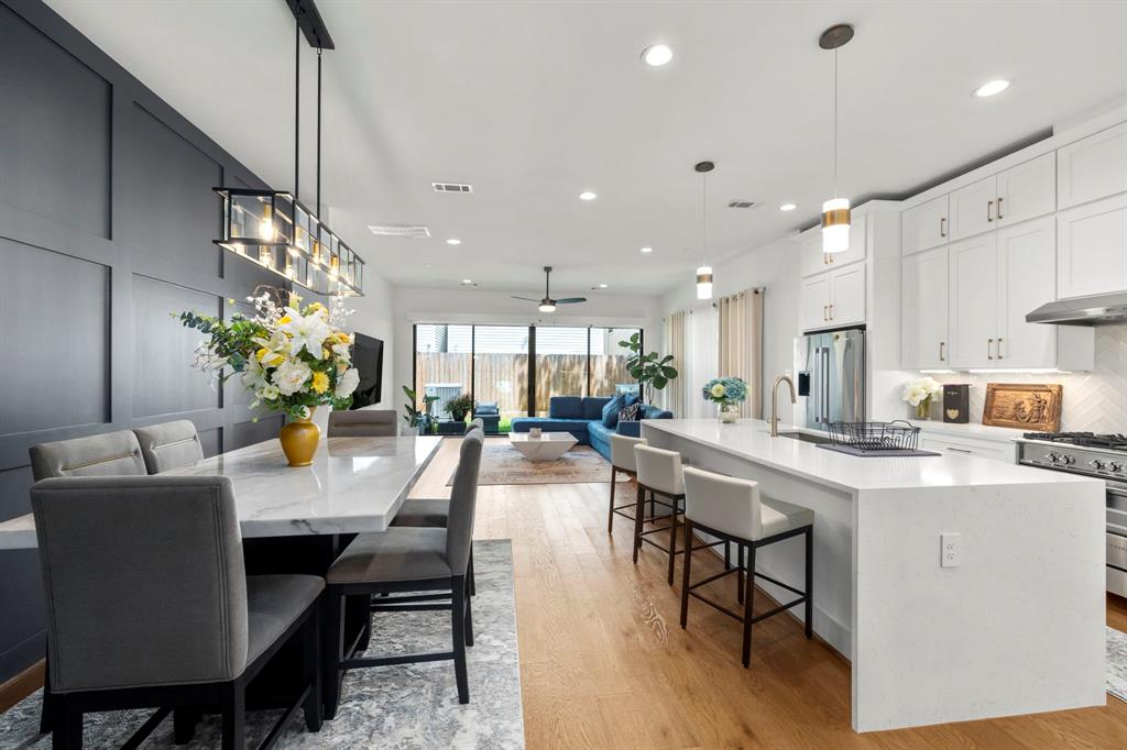 This beautifully designed open-concept kitchen and living area features a stunning oversized island with quartz countertops, sleek white cabinetry, and modern pendant lighting. The adjacent dining space, framed by a chic accent wall, is perfect for both casual meals and formal gatherings, while large windows fill the room with natural light, offering seamless indoor-outdoor flow.