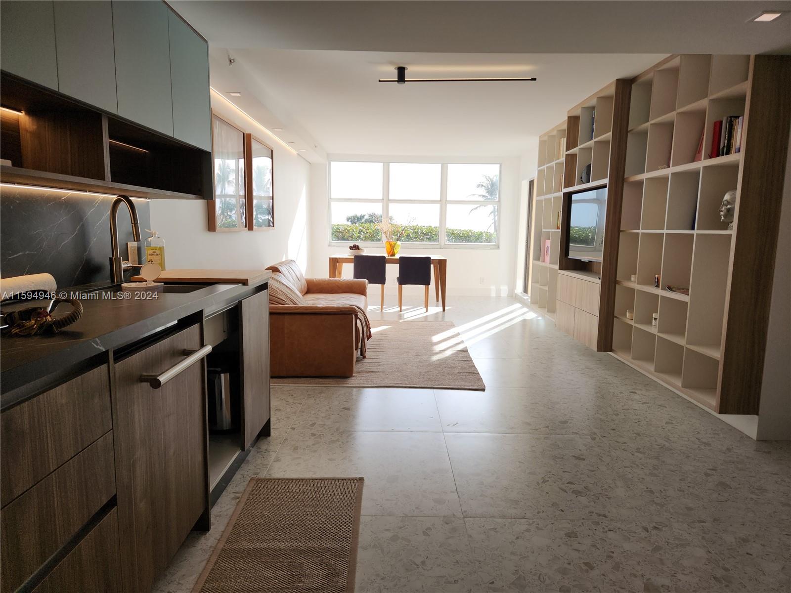 a living room with stainless steel appliances furniture a flat screen tv and a window