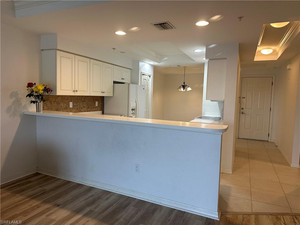 Kitchen with kitchen peninsula, white refrigerator with ice dispenser, hanging light fixtures, white cabinets, and light wood-type flooring