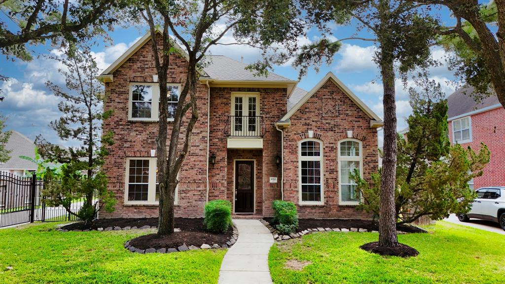 This is a two-story, brick-faced home with large windows and a welcoming front entrance. It's nestled between mature trees and has a neatly manicured lawn with a pathway leading to the front door.